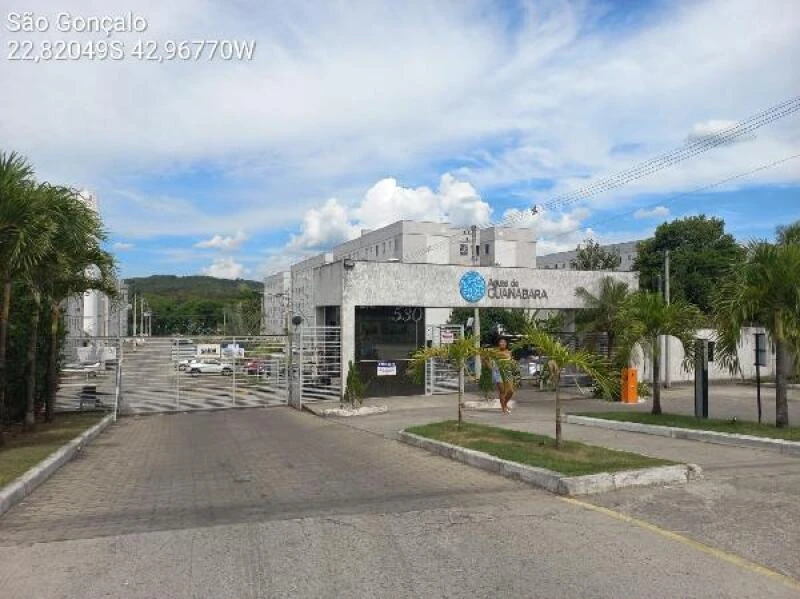 Apartamento branco em condomínio residencial com portaria e área verde localizada em São Gonçalo com céu parcialmente nublado