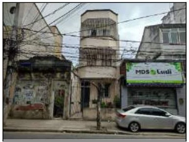 Apartamento residencial claro com varanda sacada na fachada localizado em área urbana com carro estacionado na frente e fiação elétrica visível