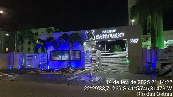 Apartamento à noite na entrada do Condomínio Residencial Parque Santiago com iluminação azul e portão metálico