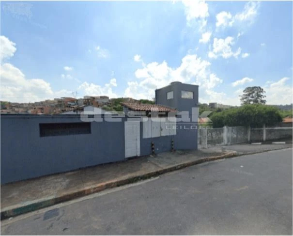 Casa azul com muro baixo e portão branco em rua residencial com calçada e céu nublado